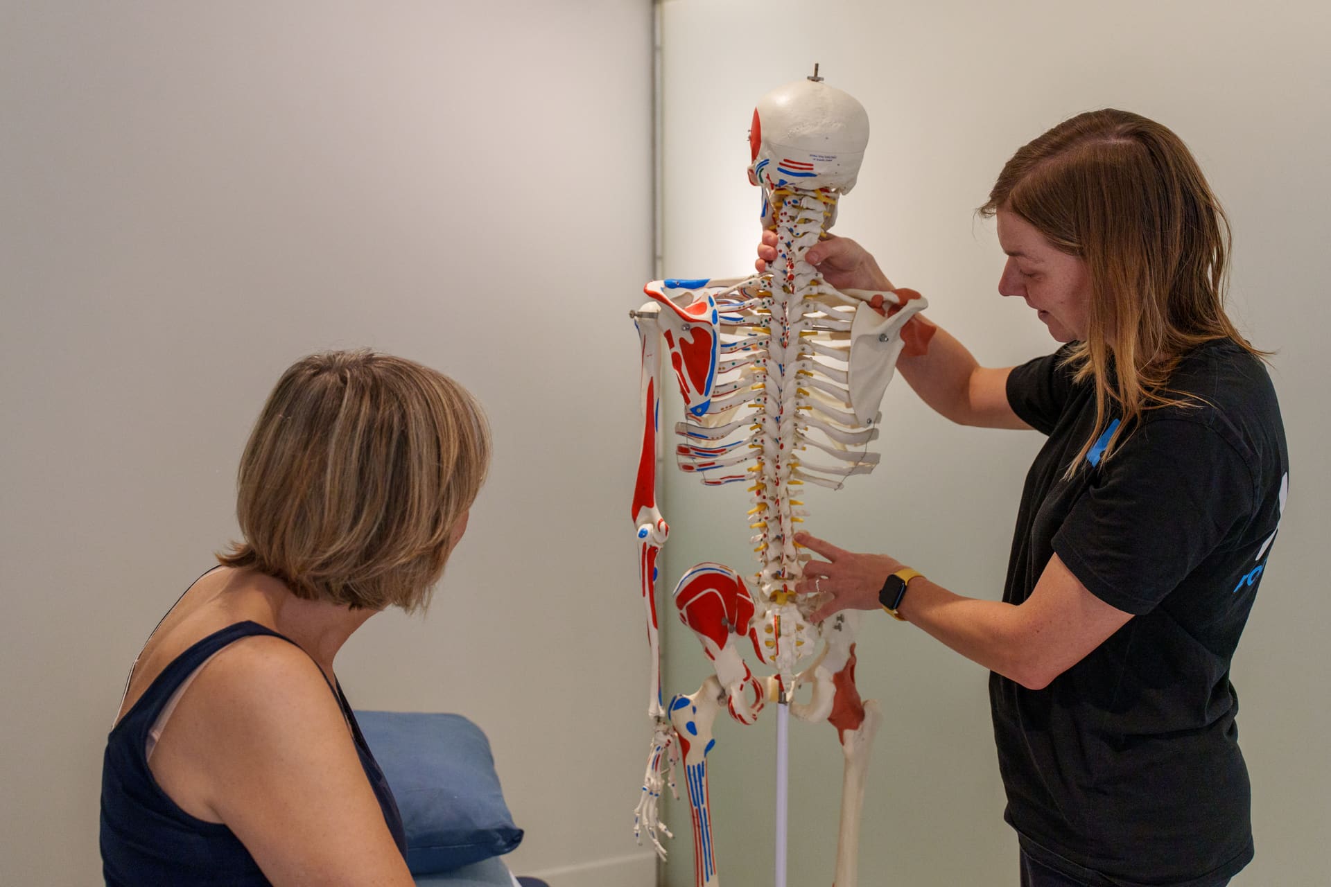 Kinesitherapeute geeft uitleg aan de hand van een wervelkolommodel tijdens de intake