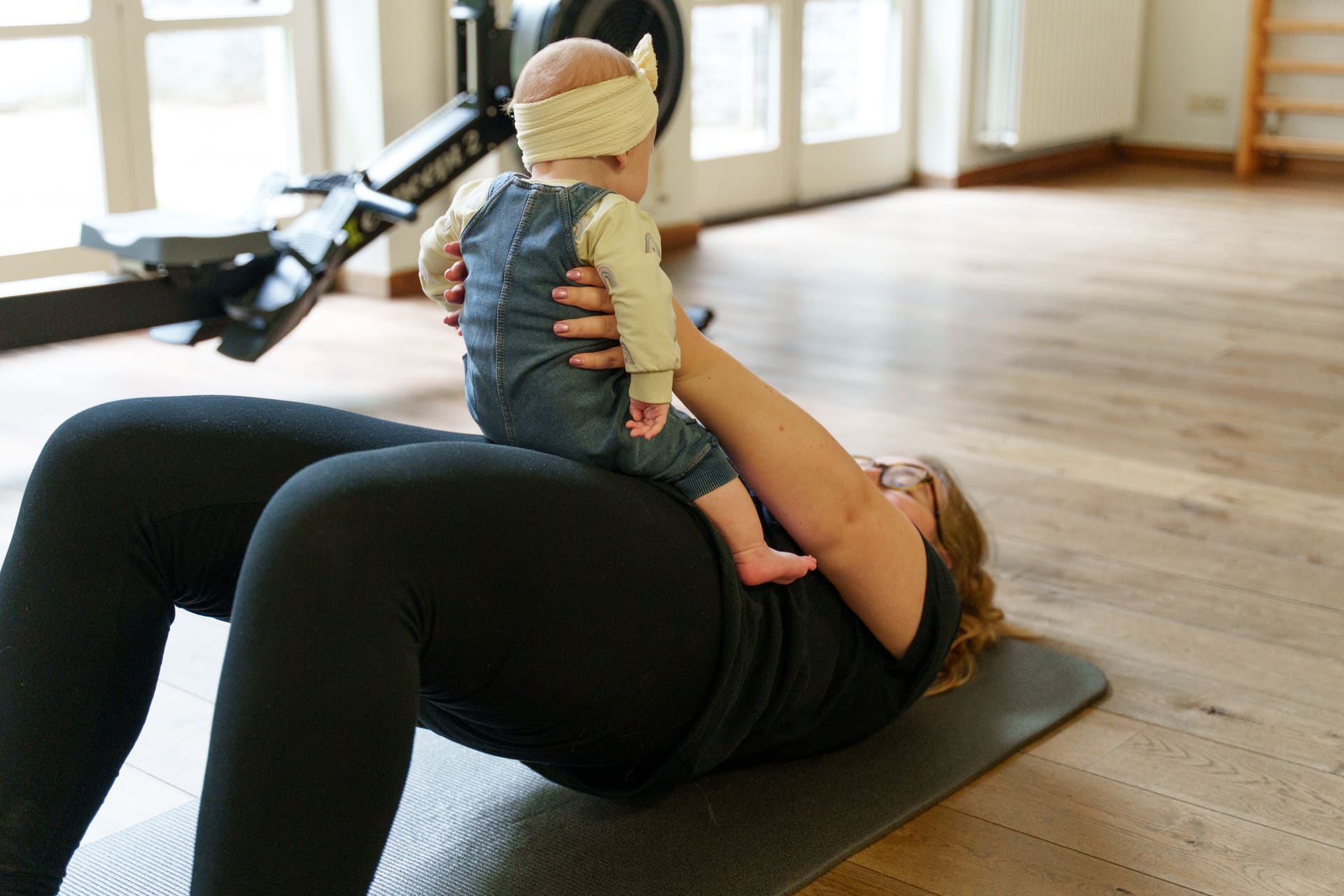 Moeder traint haar buikspieren op de mat en tilt daarbij haar baby op